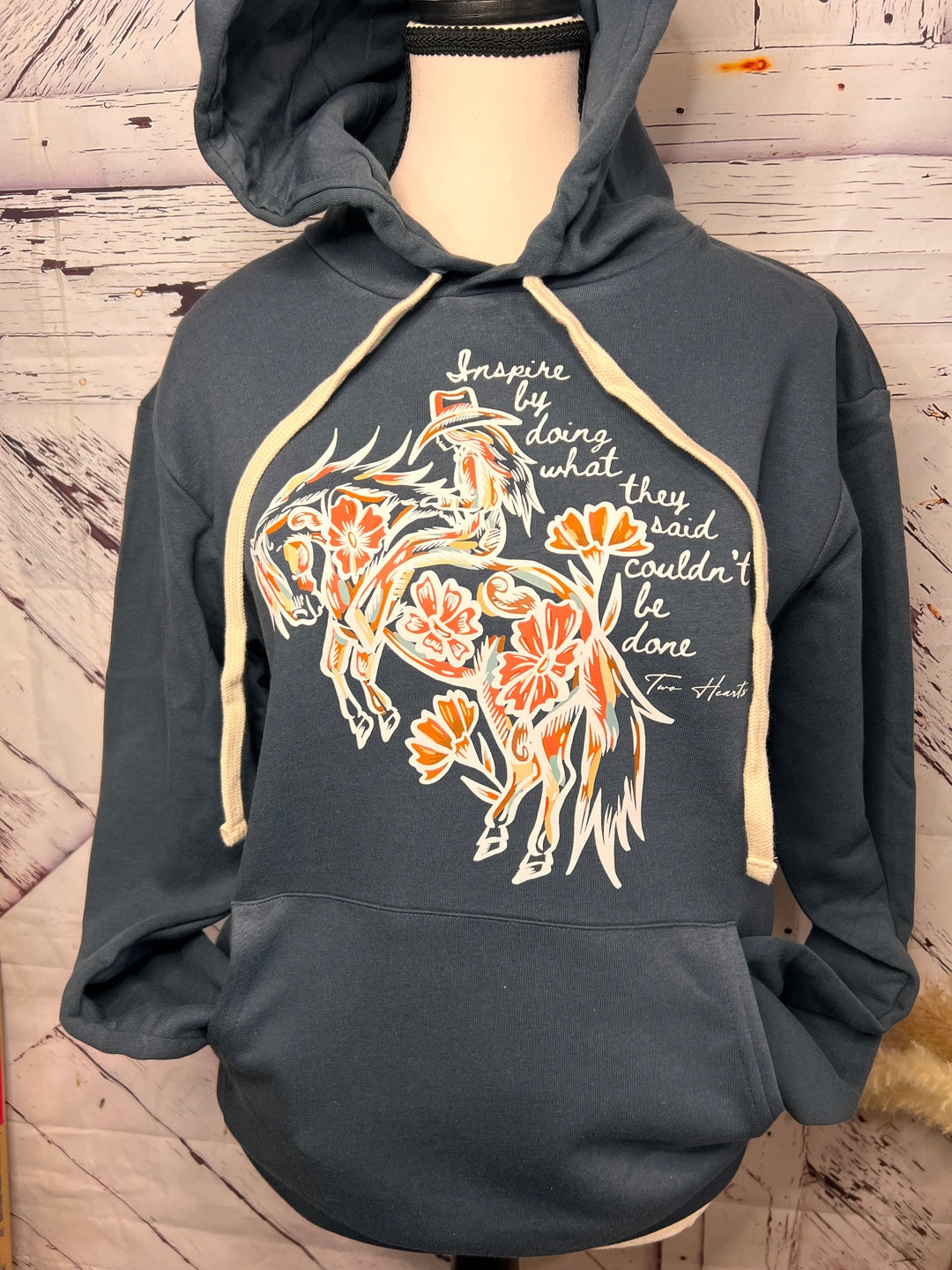 A steel blue hoodie with a front graphic design of a floral cowgirl on horseback and text quote.