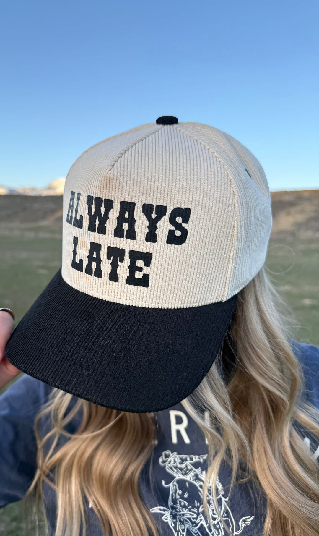 A person wearing a beige and black ballcap with the text 'ALWAYS LATE' printed on the front.