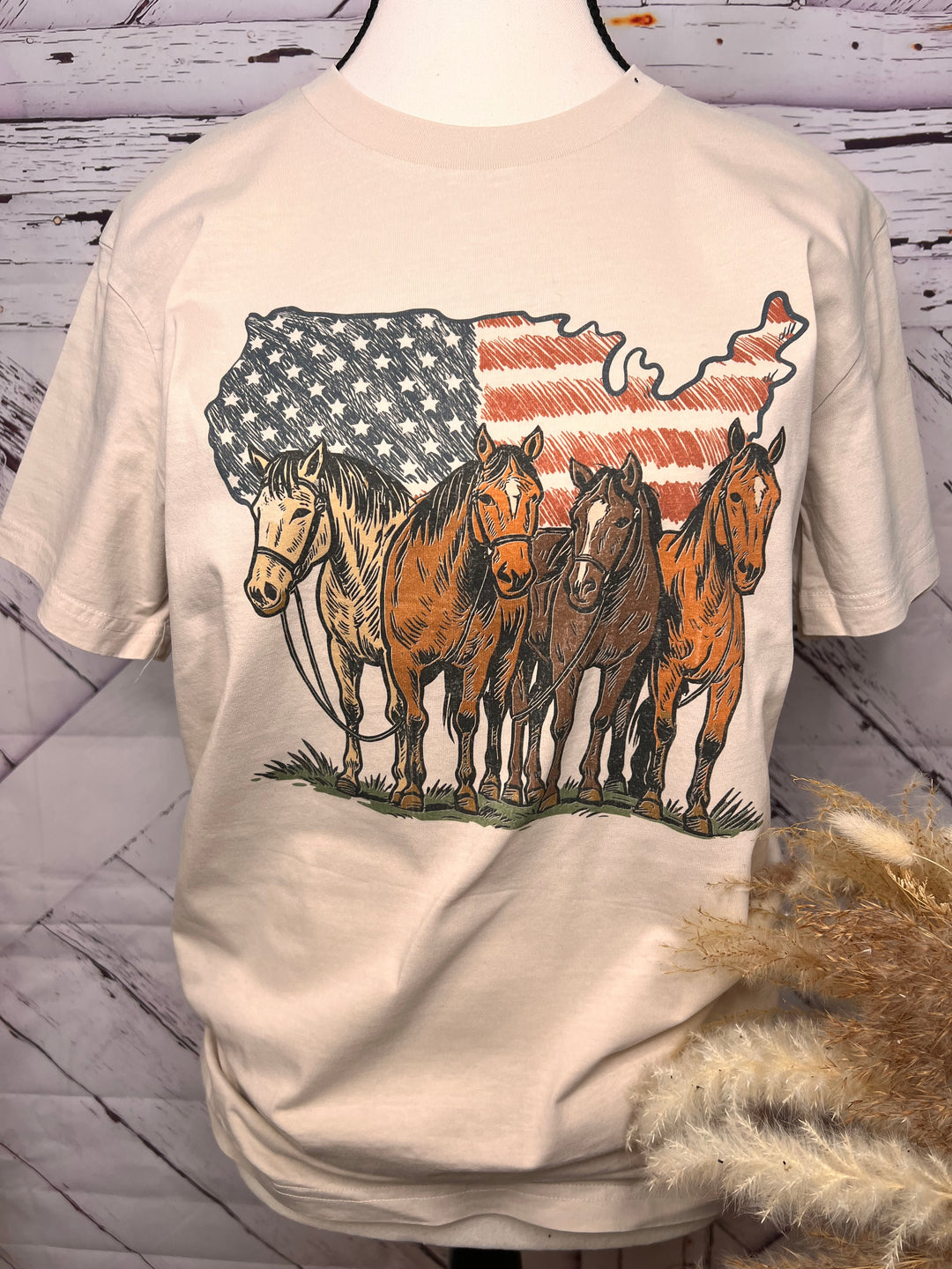 Beige sweatshirt with horse and American flag design on a wooden surface