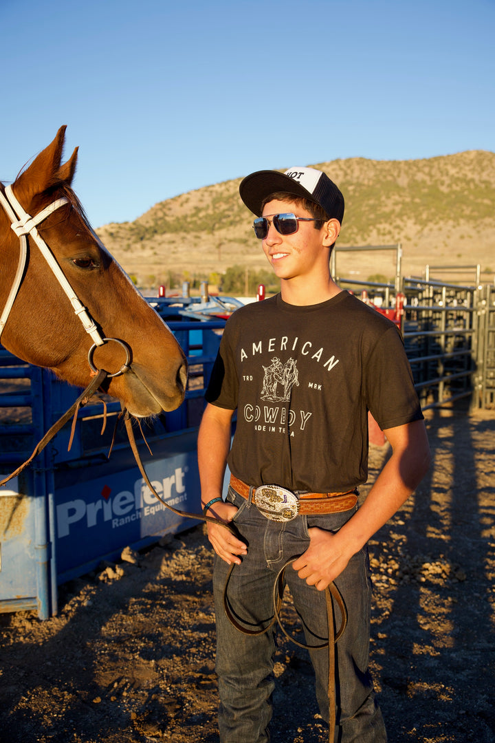 A man standing next to a brown horse, wearing a black graphic tee with &