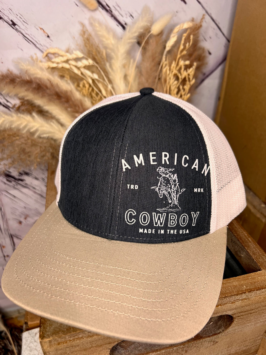 A black and beige 'American Cowboy' trucker ballcap with a logo and text on the front.