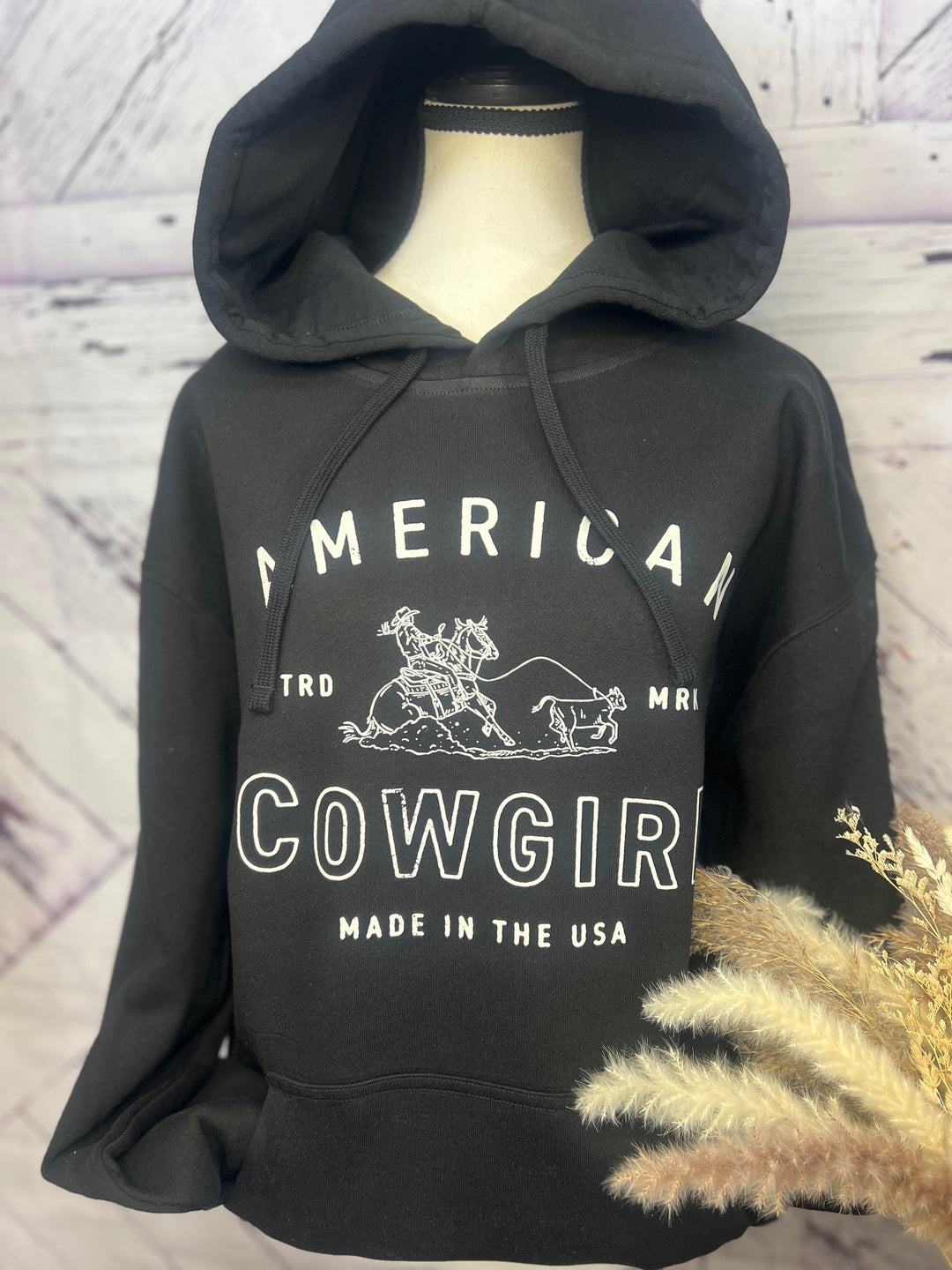 Black hoodie with 'American Cowgirl' text and a graphic of a cowgirl roping a calf.