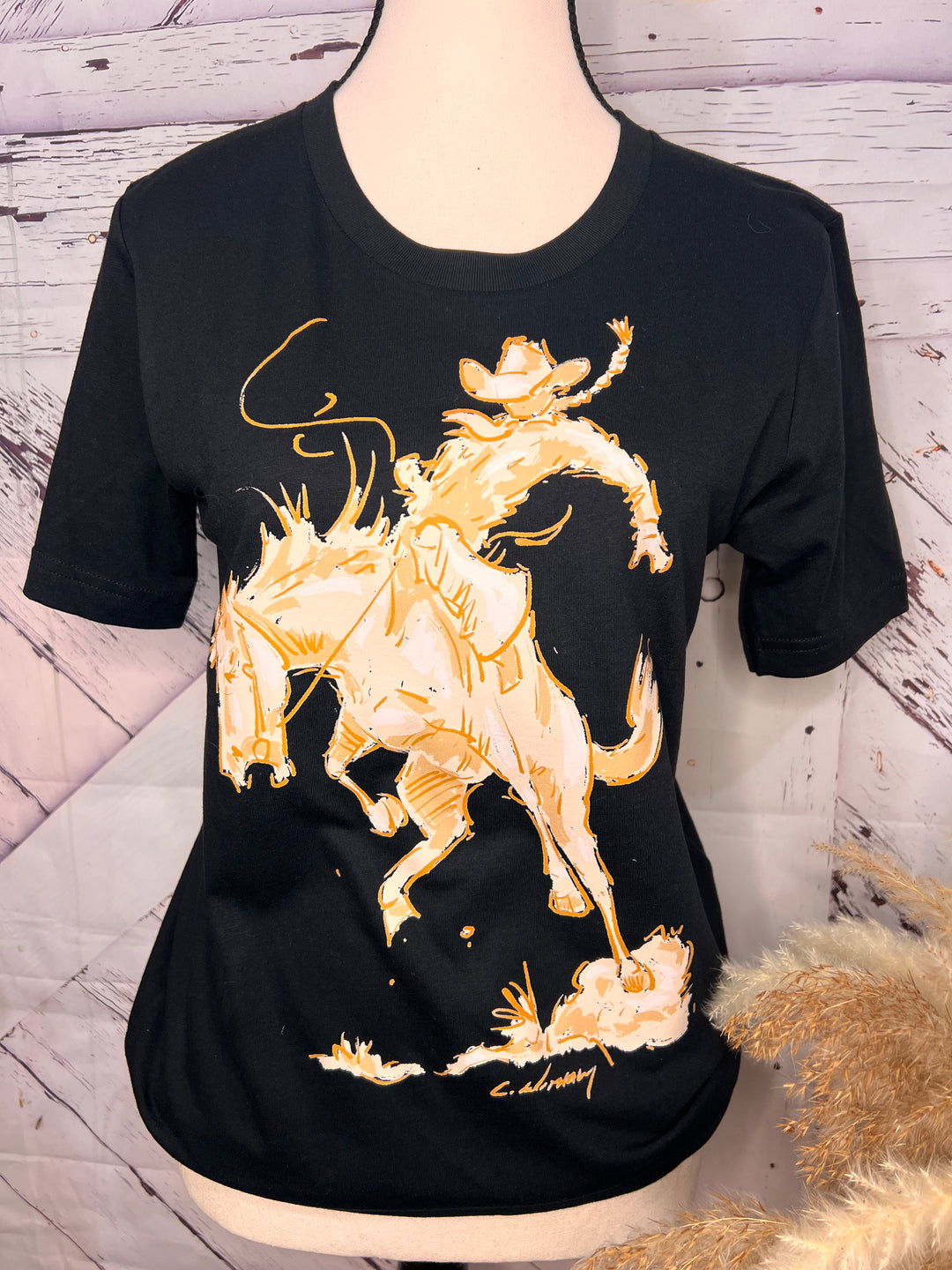 A person wearing a black t-shirt with a white and tan silhouette graphic of a cowgirl riding a bronc horse.
