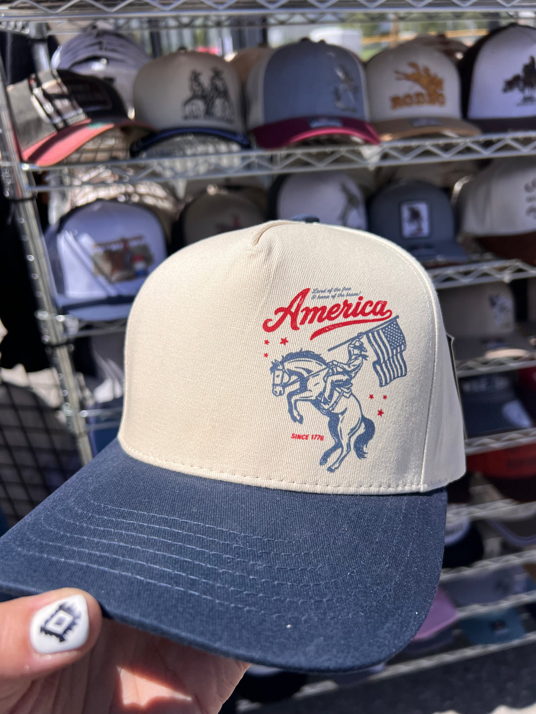 Cap with 'America' and horse design held in front of a rack of similar caps.