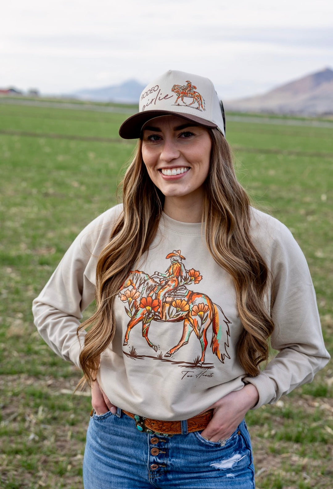 Woman wearing a cap and long-sleeve shirt with a horse design in an open field.