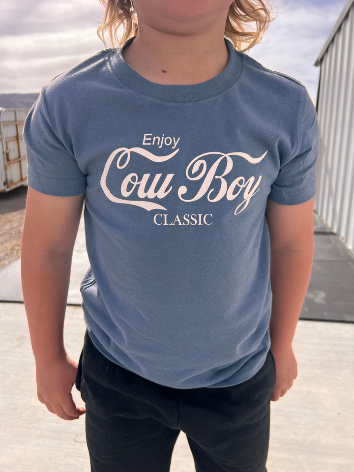 A person standing next to a horse inside a stable, wearing a gray graphic tee with the text &