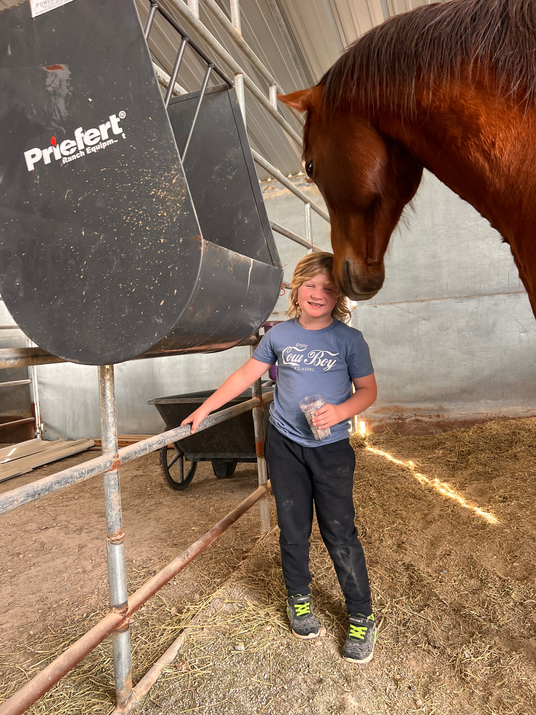 A person standing next to a horse inside a stable, wearing a gray graphic tee with the text &