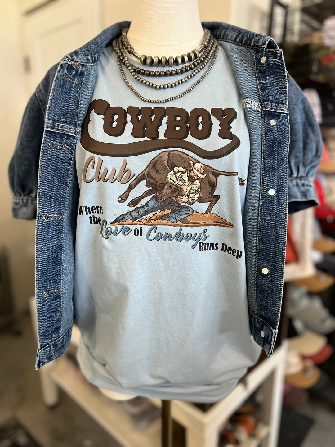 Mannequin wearing a denim jacket over a t-shirt with a cowboy graphic and text.