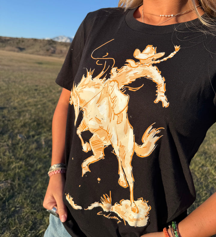 Person wearing a black t-shirt with a gold horse graphic in a natural setting.