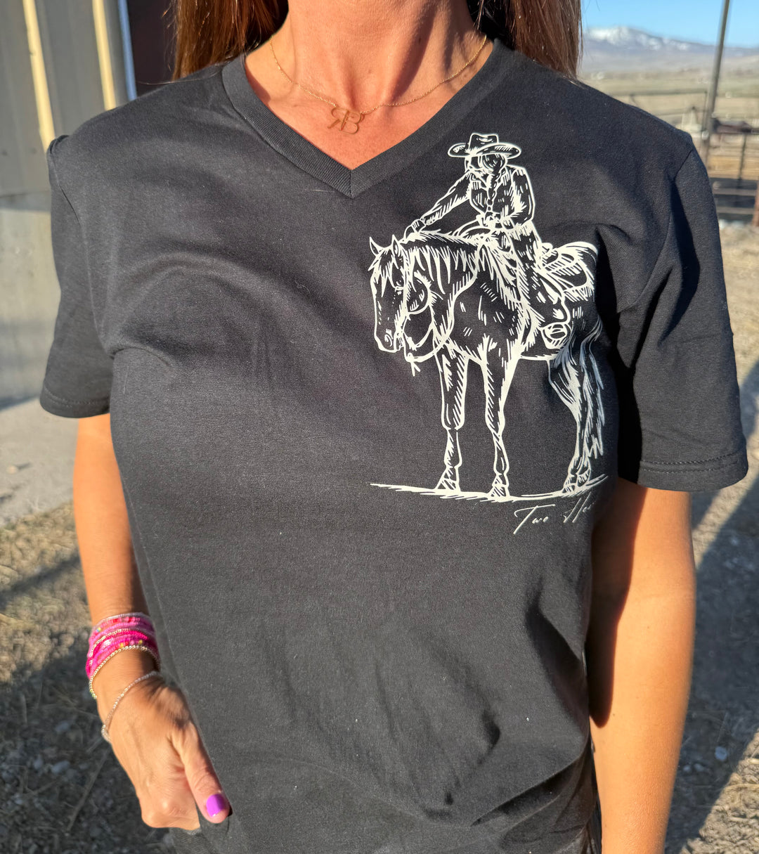 A person wearing a black V-neck tee with a graphic of a cowgirl reaching up to pat a horse&