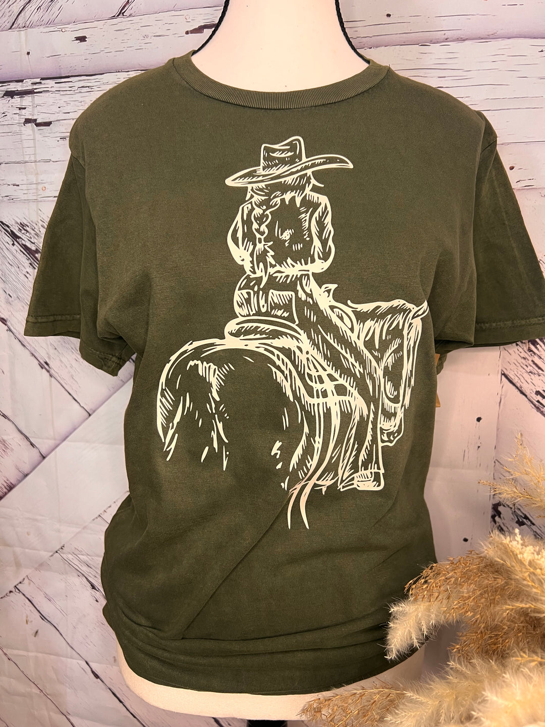 A green t-shirt with a white print of a cowgirl riding a horse.