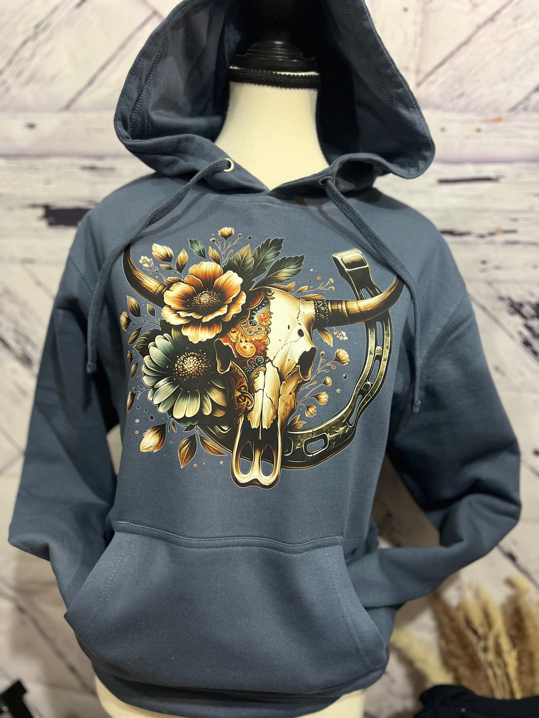 A stone blue hoodie with a decorated steer skull design featuring flowers and a horseshoe printed on the front.
