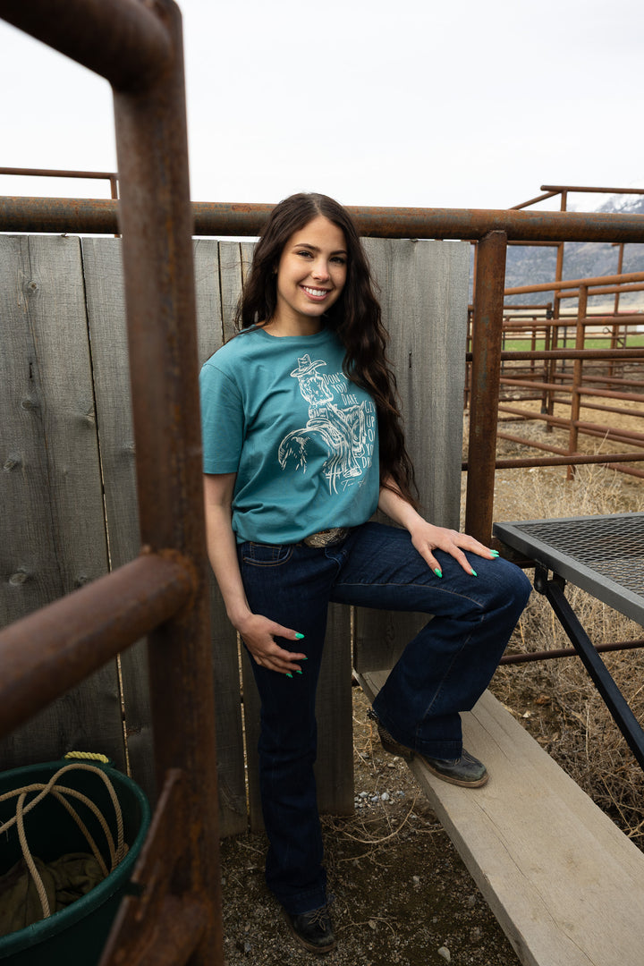 Woman in a blue shirt sitting on a wooden structure with a fence and field in the background