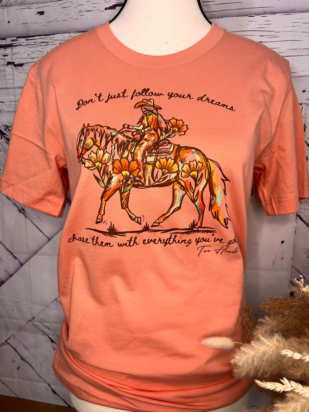 Peach t-shirt with graphic design and text on a wooden surface.