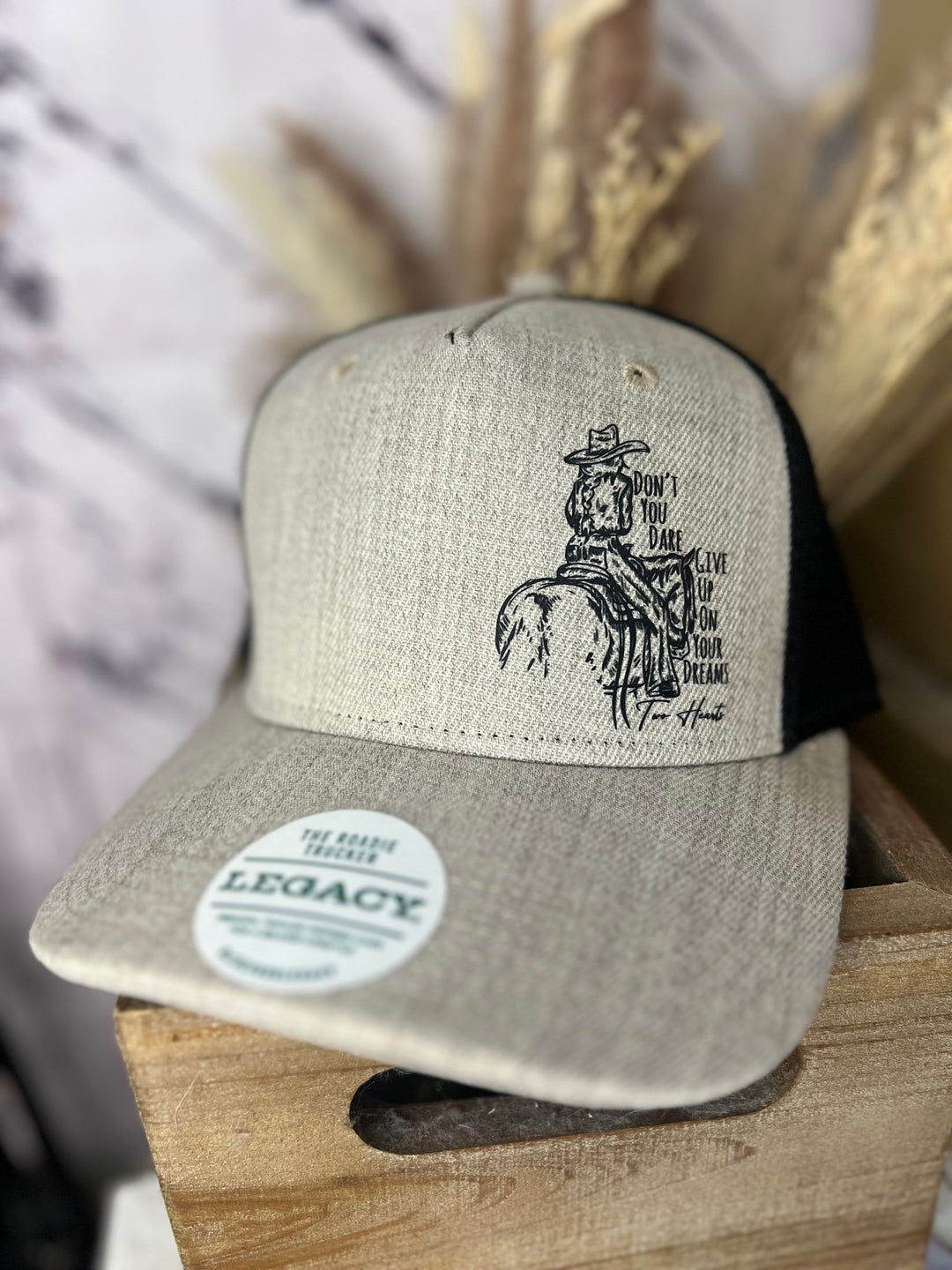 A navy and beige ballcap with a cowgirl riding a horse design, and a patterned brim, placed on a wooden surface.