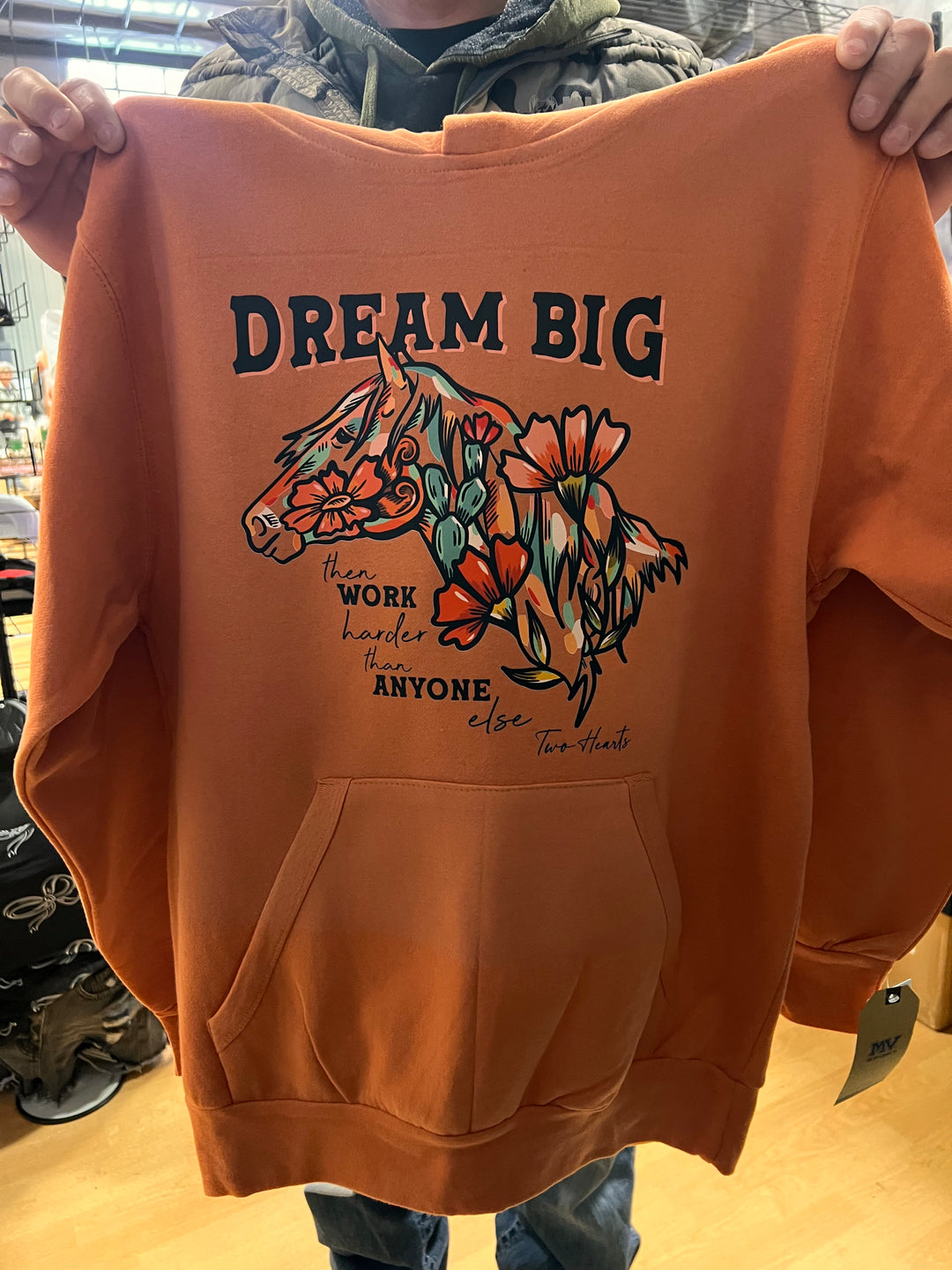 Orange sweatshirt with floral design and text held by a person.