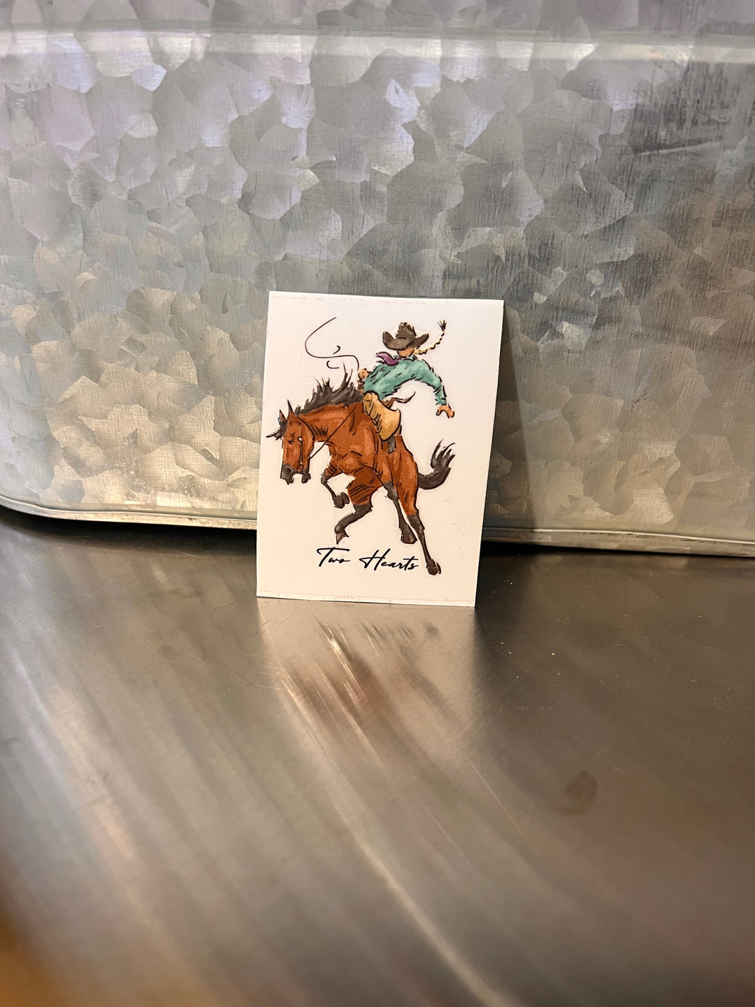 Small card with a drawing of a person riding a horse on a metallic surface