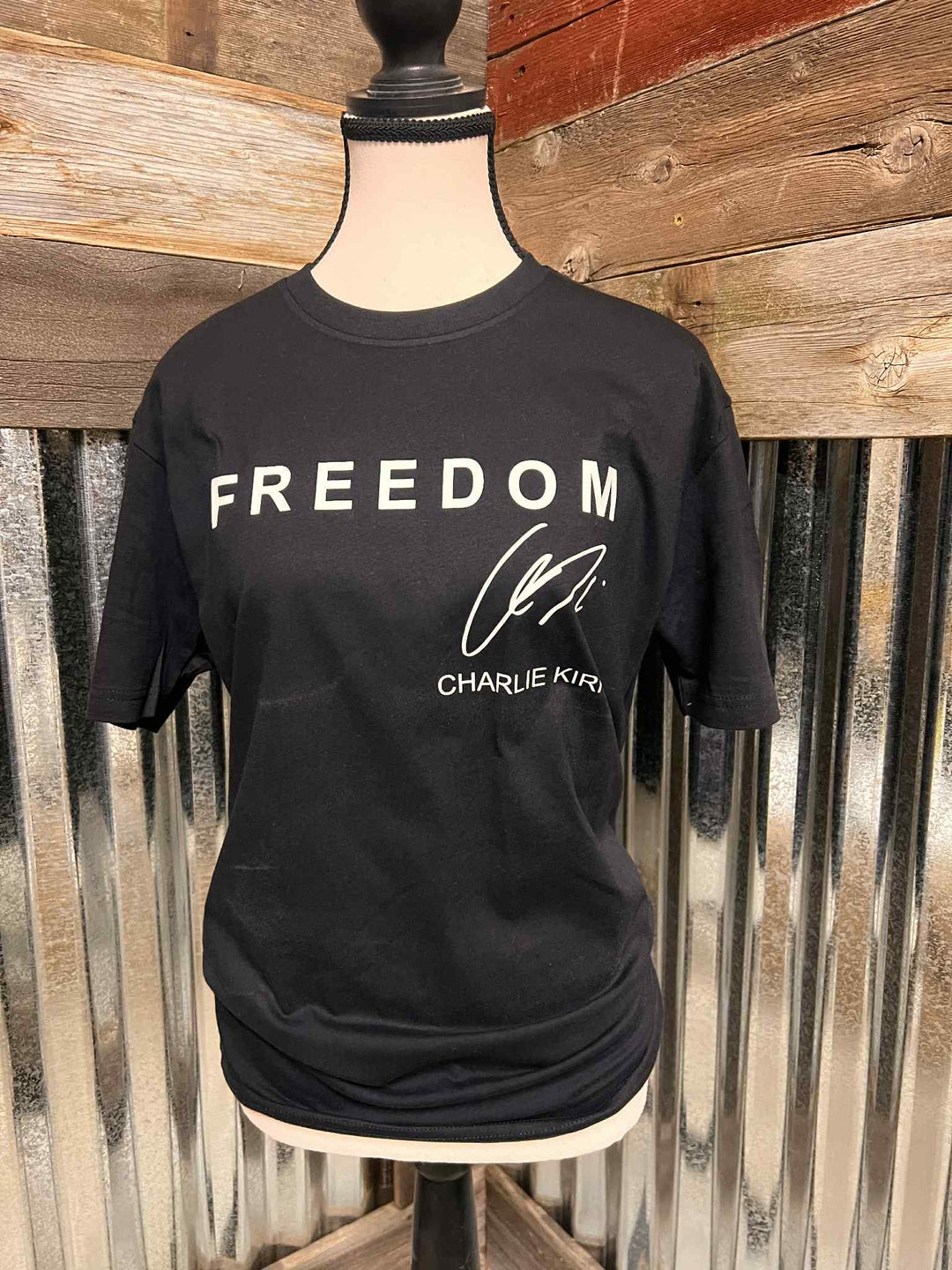 Black t-shirt with 'FREEDOM CHARLIE KIRK' text on a mannequin against a rustic wooden background