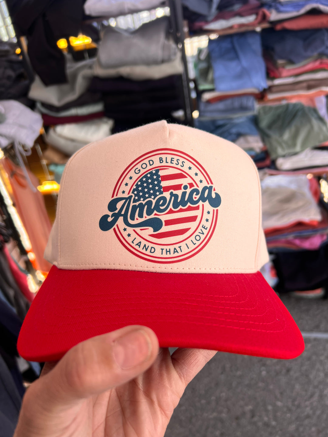 Cap with 'America' design held in front of a clothing rack