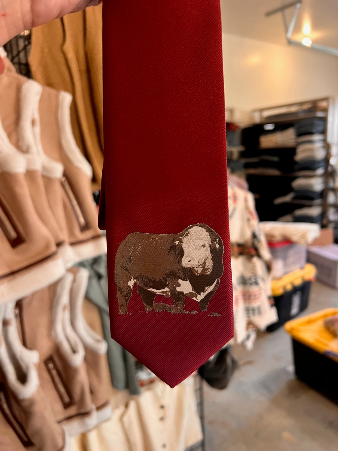 Red tie with a dog design held in front of a clothing rack.