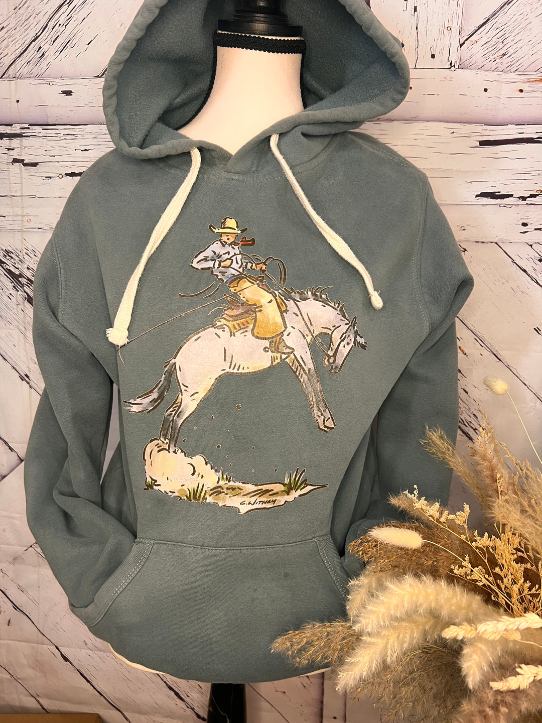 A gray hoodie featuring a western graphic hoodie/crewneck design with a cowboy and a bucking horse.
