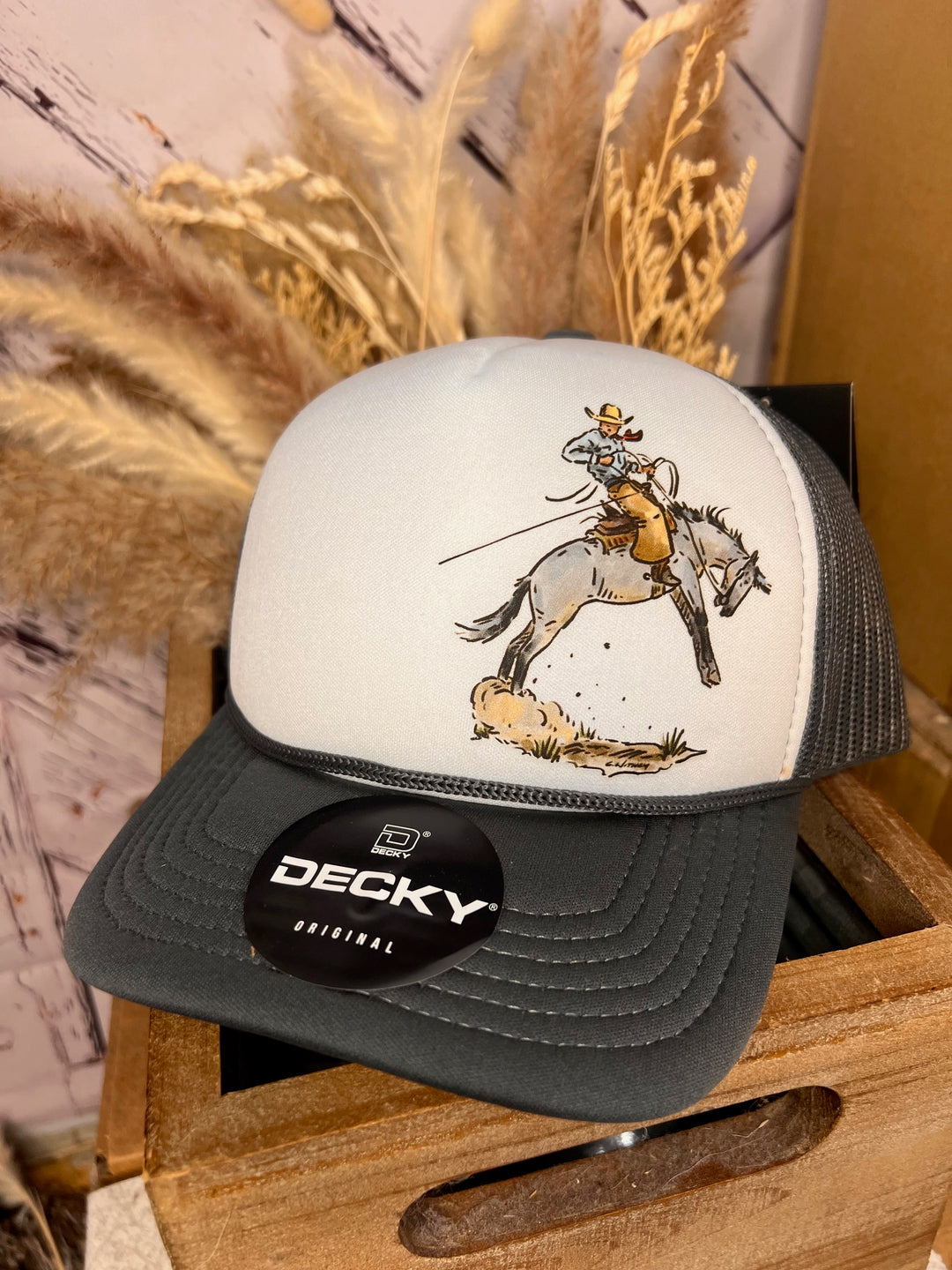 A black and white 'High Line' cowboy ballcap with a hand-drawn graphic of a cowboy on horseback, displayed on a wooden surface.