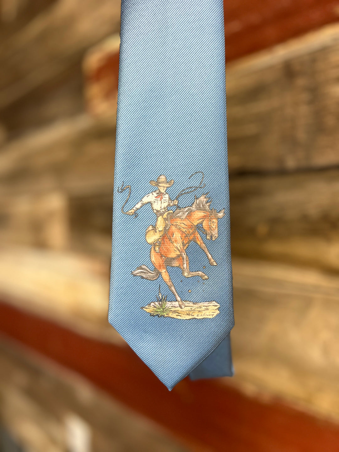 Light blue tie with a cowboy and horse design on a wooden surface