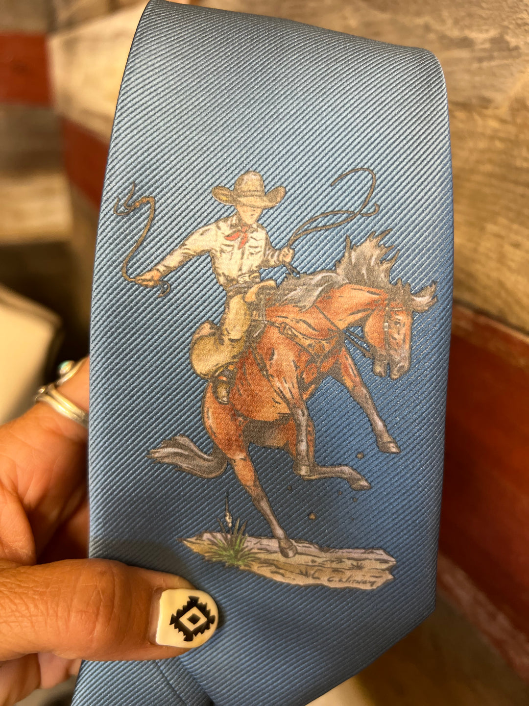 Blue fabric with a cowboy riding a horse design held by a hand.