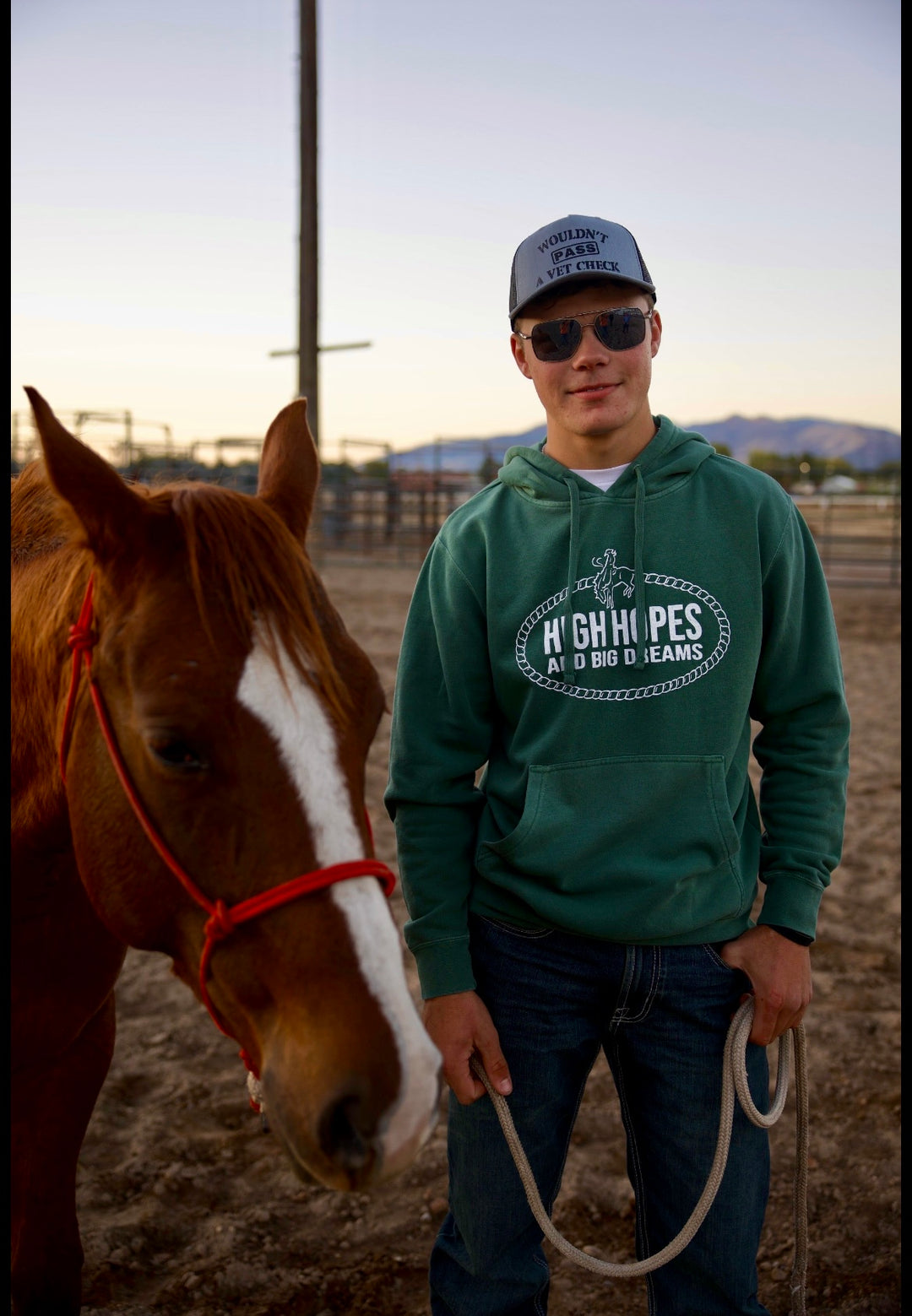 A person standing next to a horse, wearing a green hoodie with a graphic of a bucking horse and the phrase 'High Hopes and Big Dreams'.