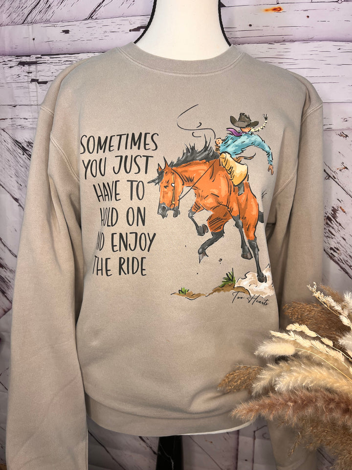 A person wearing a gray crewneck sweatshirt with a hand-drawn illustration of a lady riding a bronc horse and the text &