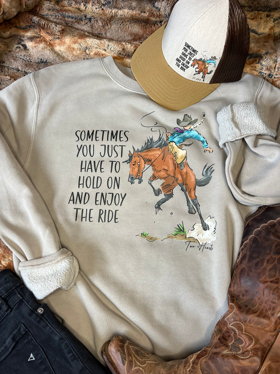 A person wearing a gray crewneck sweatshirt with a hand-drawn illustration of a lady riding a bronc horse and the text &