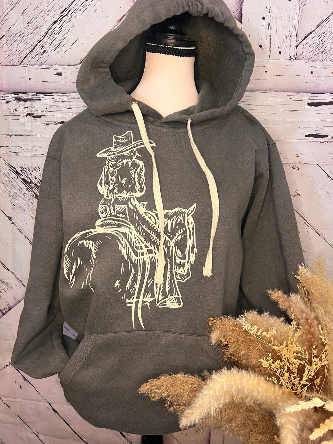 A gray hoodie featuring a printed design of a cowgirl riding a horse, displayed on a mannequin.
