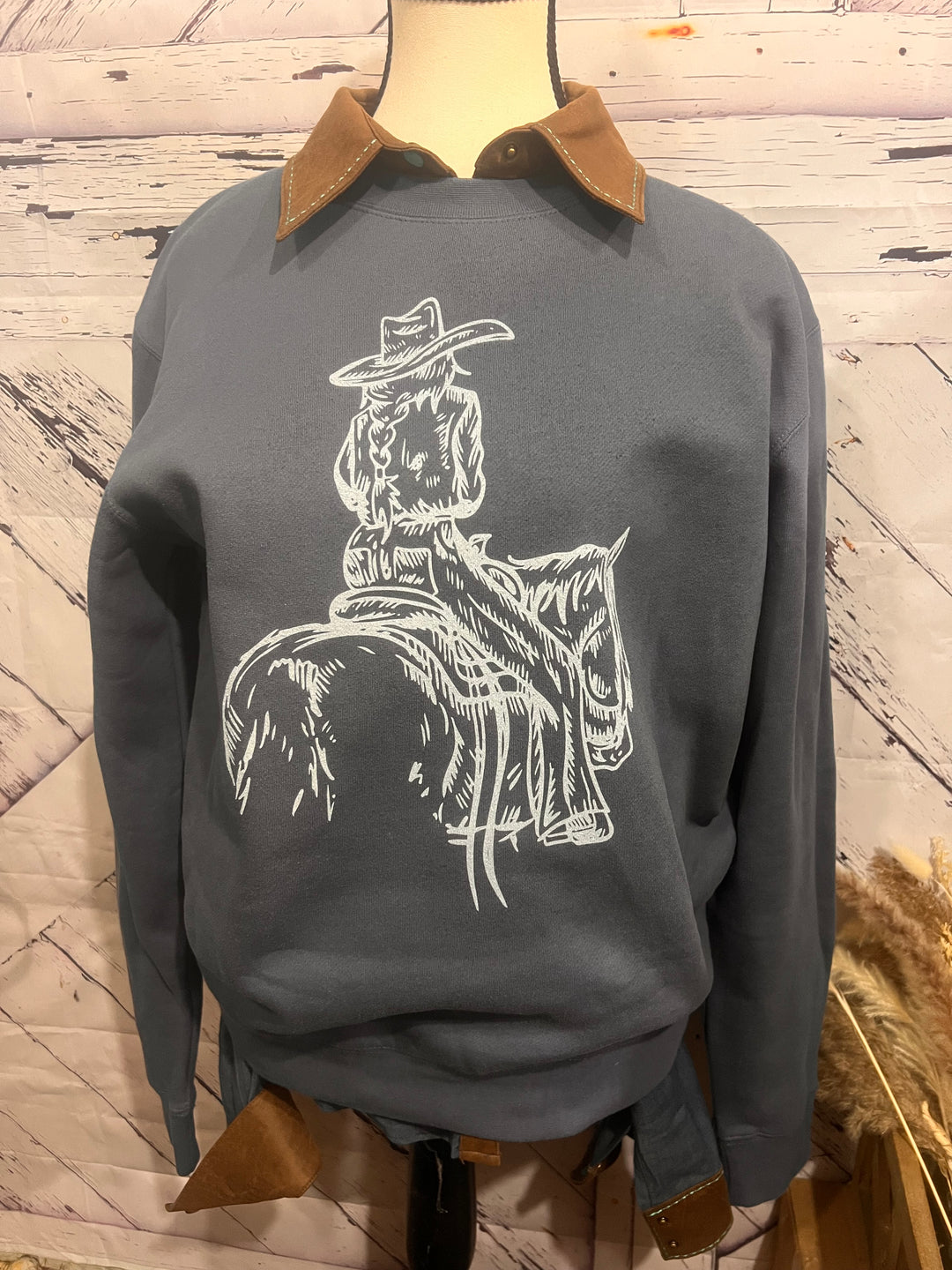 A stone blue sweatshirt with a graphic of a cowgirl riding a horse in a soft white print.