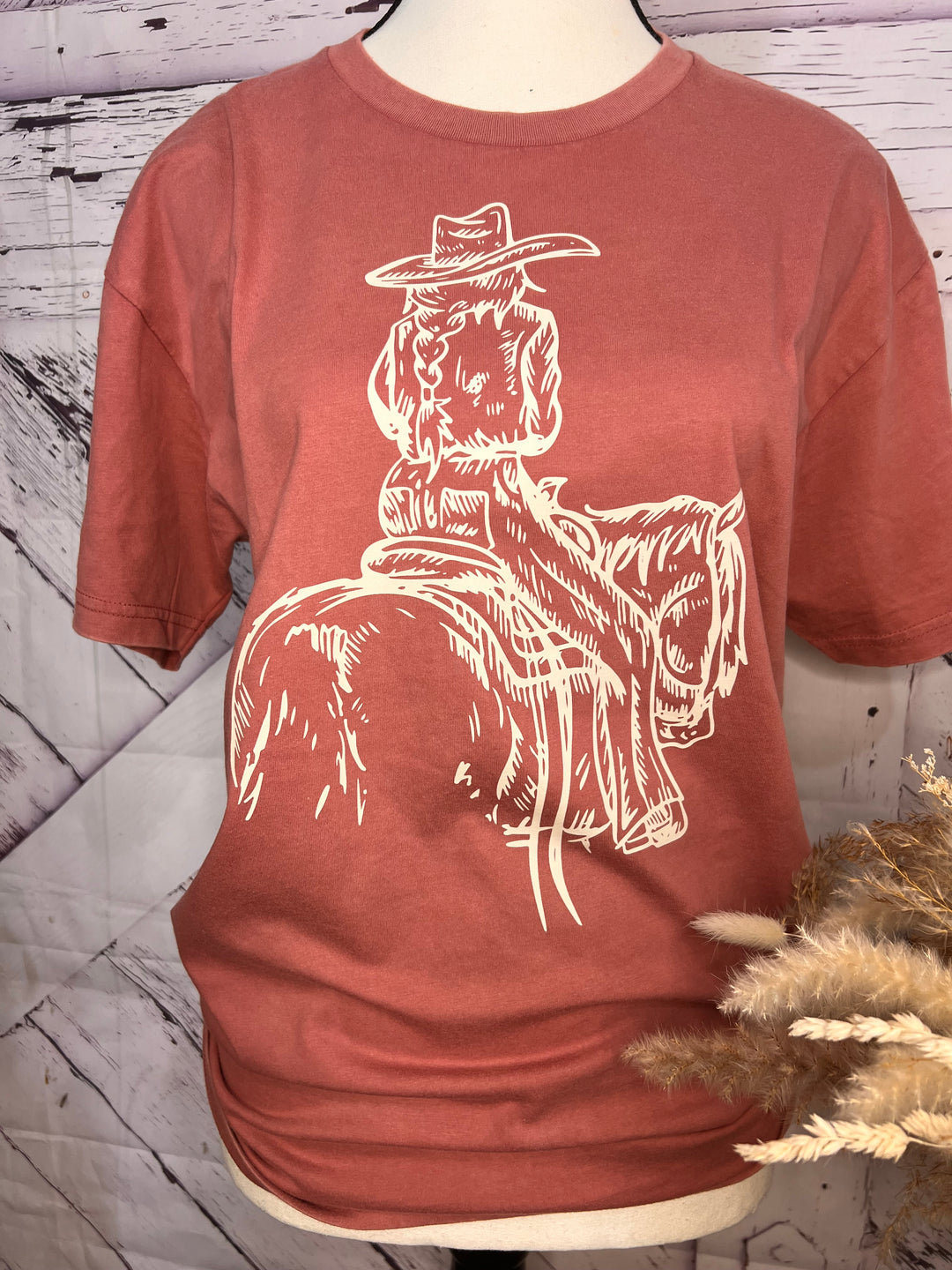 A pink t-shirt with a white hand-drawn sketch of a cowgirl riding a horse.