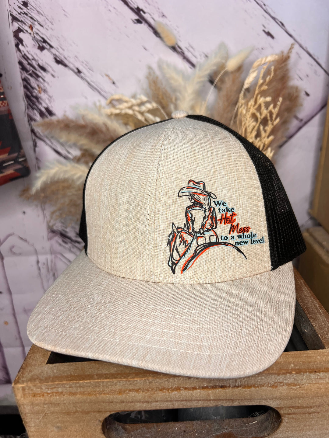 A beige and black cowgirl ballcap with a hand-drawn cowgirl illustration and text on the front.