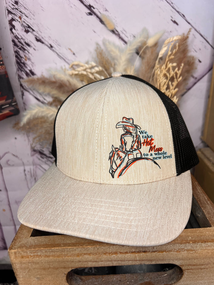 A beige and black cowgirl ballcap with a hand-drawn cowgirl illustration and text on the front.