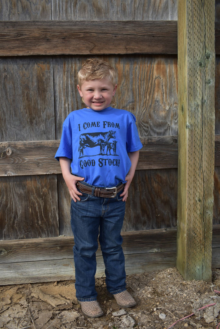 A child standing by a wooden fence, wearing a blue t-shirt with the phrase &