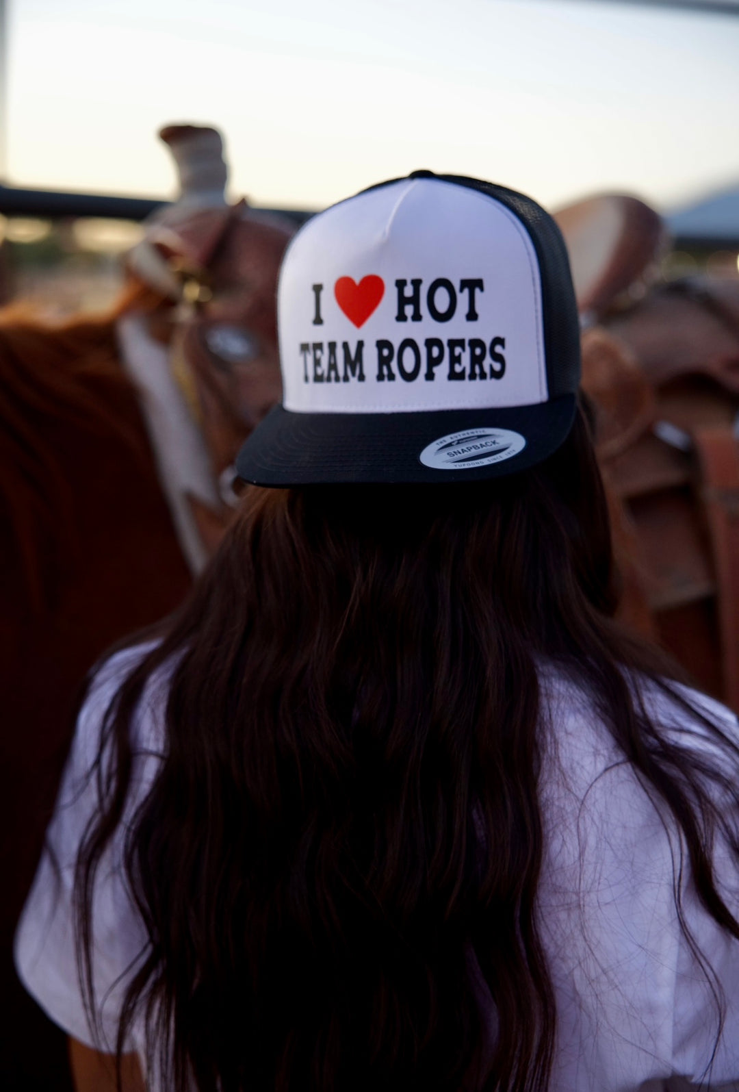 A ballcap with the text 'I ❤· HOT TEAM ROPERS' on it, worn by a person with long hair.