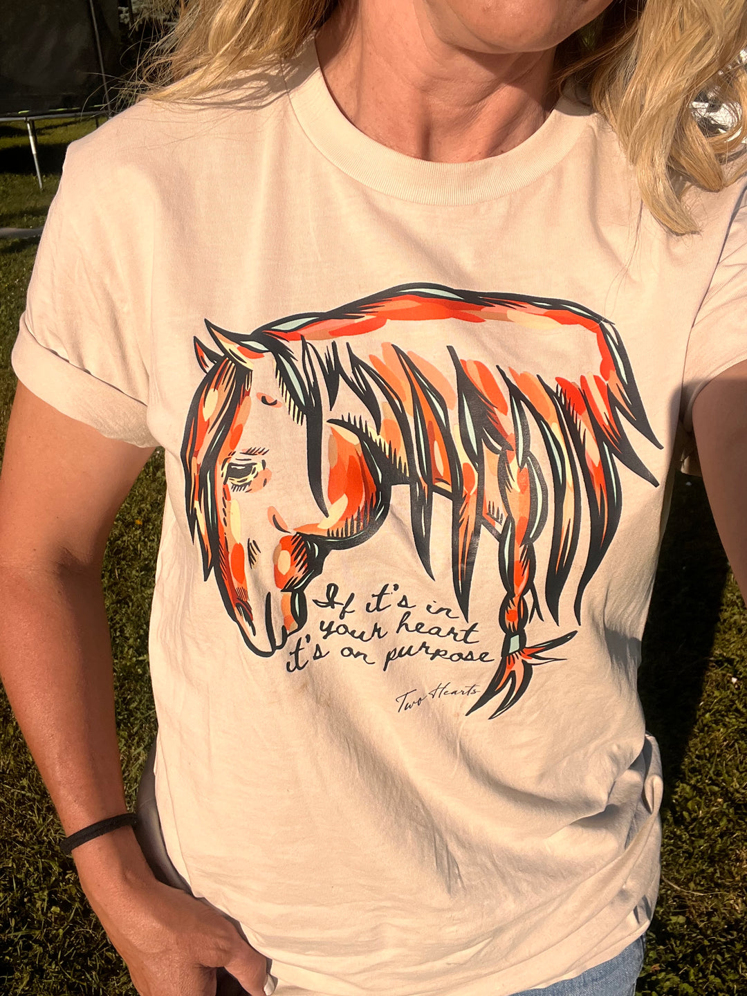 Person wearing a shirt with a colorful horse design and text outdoors.