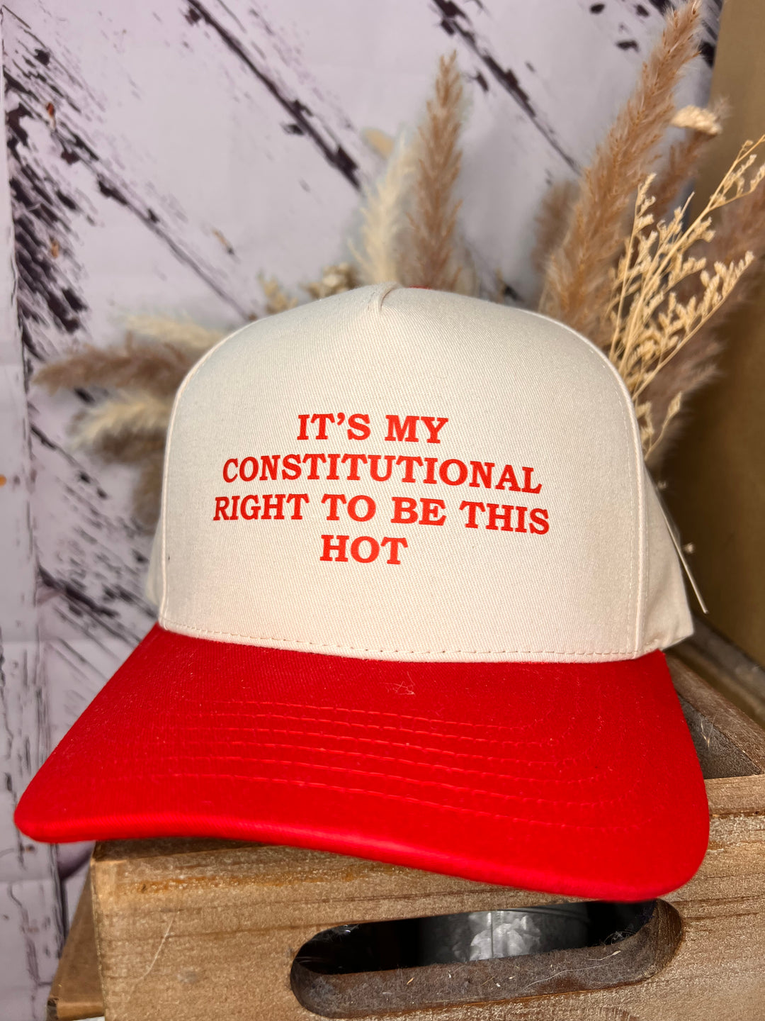 A ballcap with a khaki top and a red bill, featuring the phrase 'IT'S MY CONSTITUTIONAL RIGHT TO BE THIS HOT' in red lettering on the front.