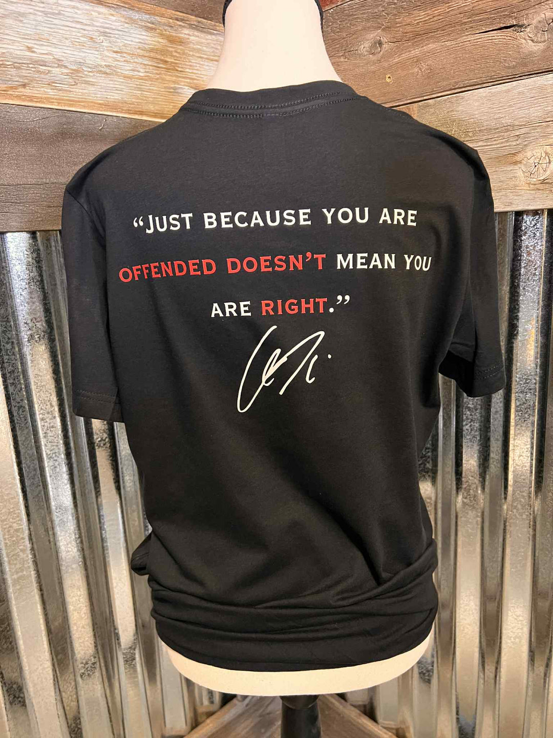 Black t-shirt with a quote on the back, displayed on a mannequin against a wooden background.