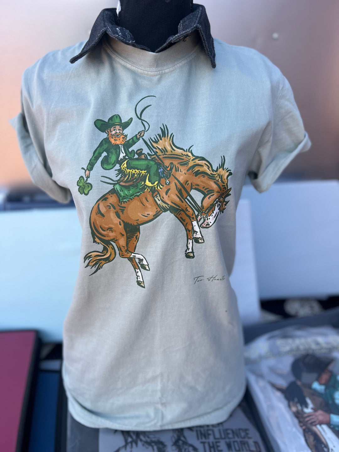 T-shirt with a graphic of a leprechaun riding a horse on a hanger.