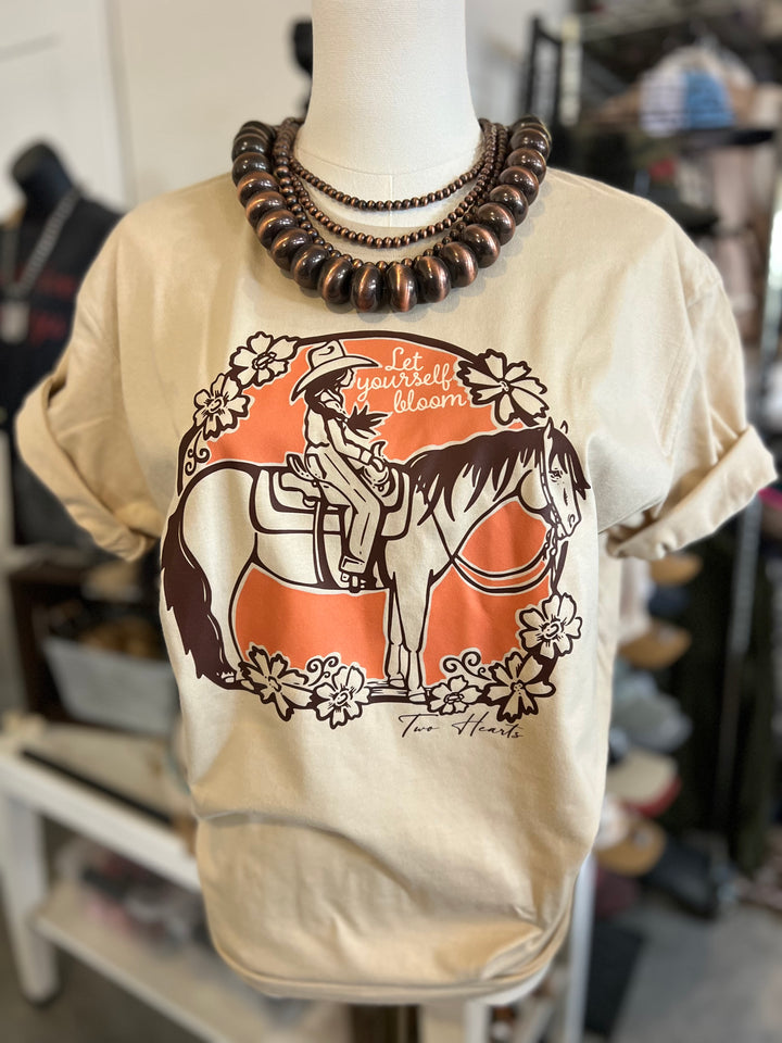 Beige t-shirt with a graphic of a cowboy on a horse and flowers, displayed on a mannequin.