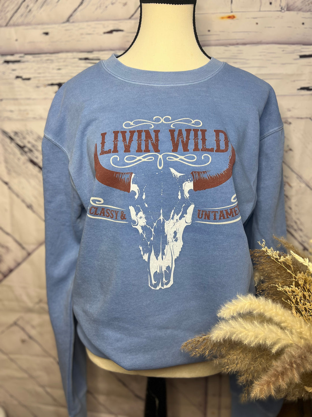 A blue crewneck sweatshirt with a graphic of a steer skull and the text 'LIVIN WILD' on the front.