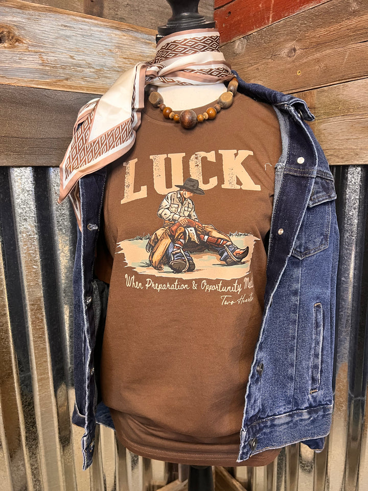 Person wearing a brown shirt with a graphic design and blue jeans, sitting on a metal surface.