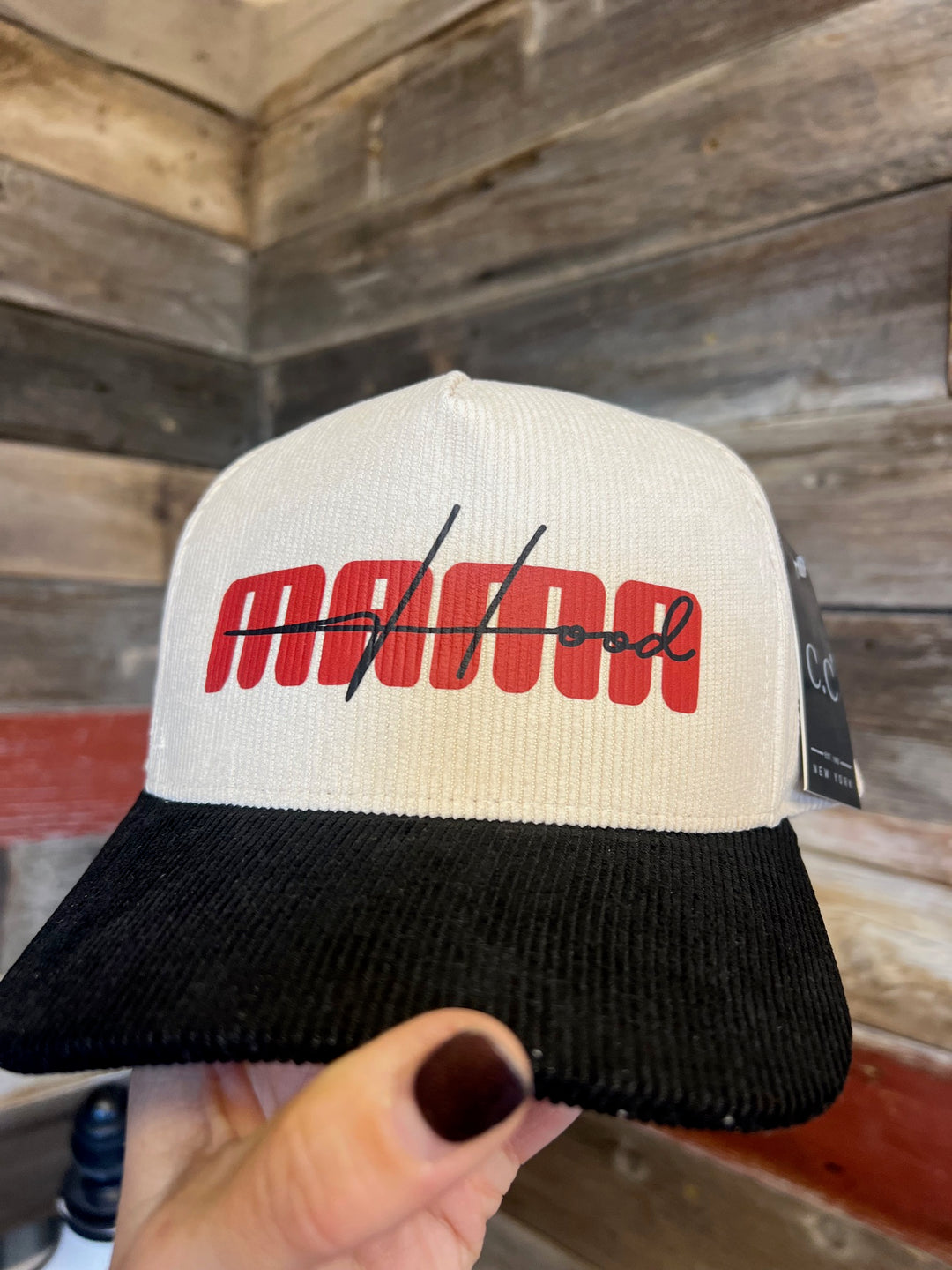 Cap with red logo held by a hand against a wooden background