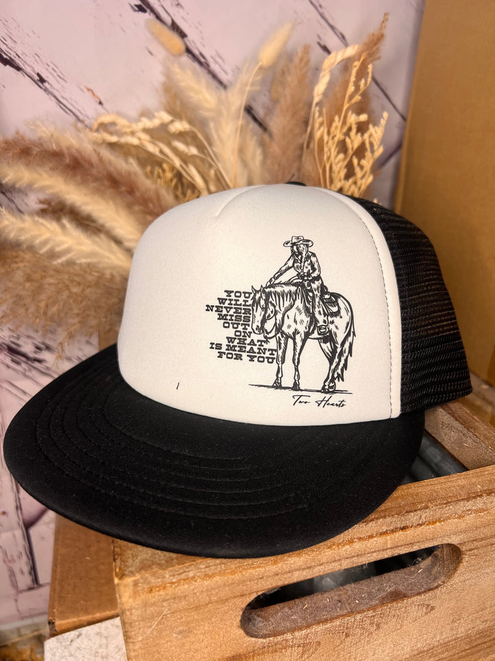 A beige and black ballcap with a graphic of a cowgirl on her horse and the text &
