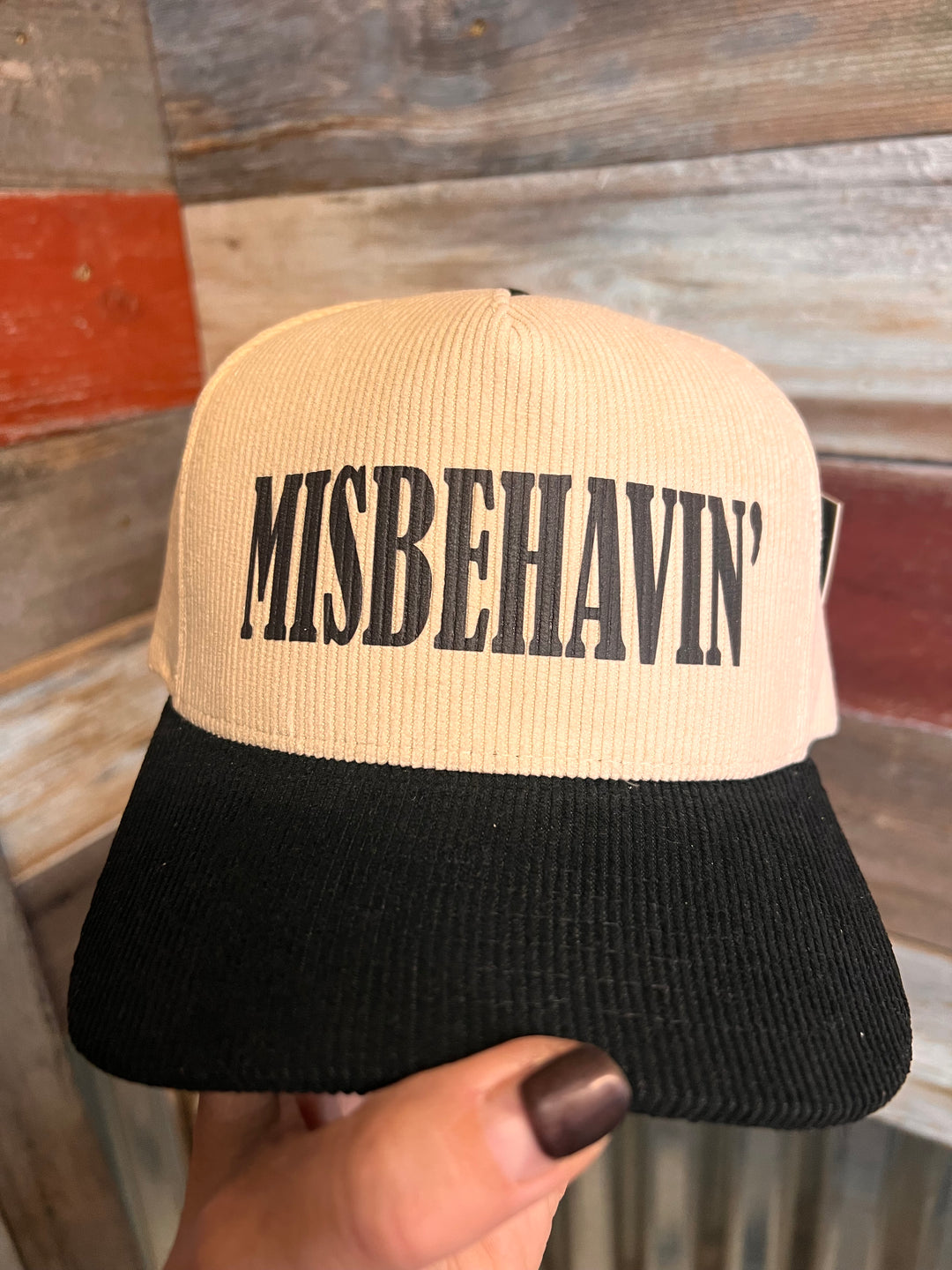 Beige and black scrunchie with 'MISBEHAVIN'' text held by a hand against a wooden background