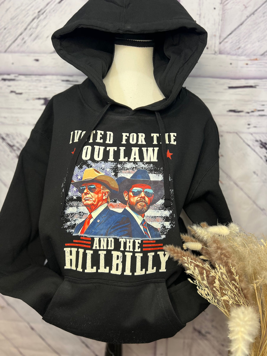 A black hoodie with a graphic print of two men wearing cowboy hats and the text 'I Voted for the Outlaw and the Hillbilly'