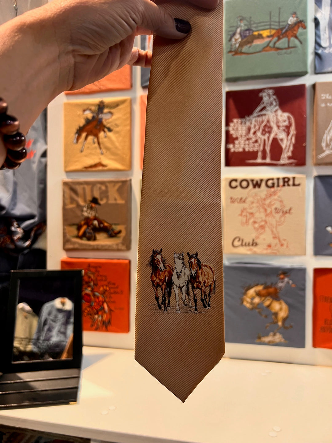 Hand holding a tie with cowboy design against a background of similar ties.